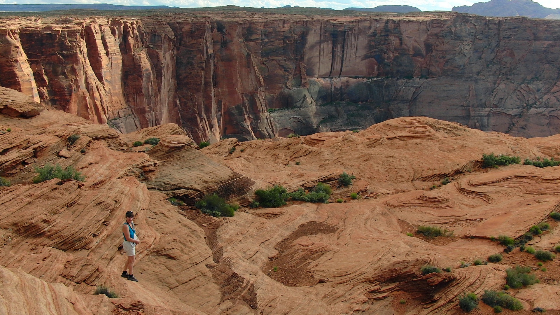 Woman in White Shirt and Blue Denim Jeans Walking on Brown Rocky Mountain During Daytime. Wallpaper in 1920x1080 Resolution