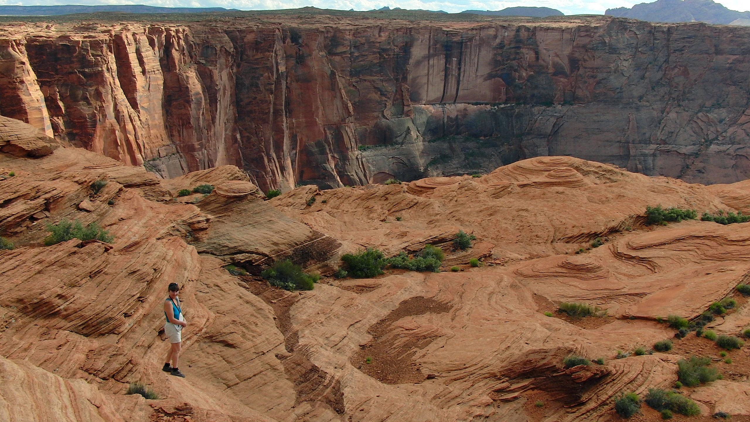 Woman in White Shirt and Blue Denim Jeans Walking on Brown Rocky Mountain During Daytime. Wallpaper in 2560x1440 Resolution
