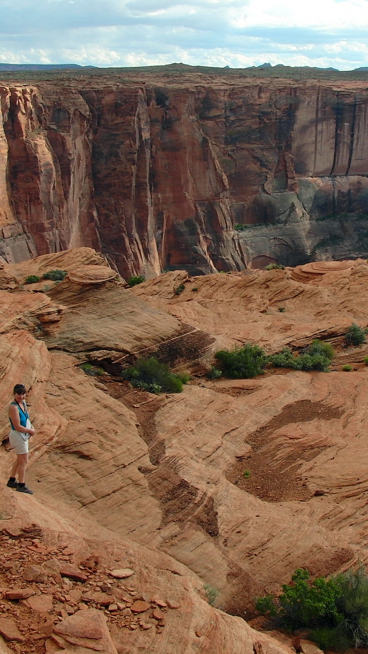 Woman in White Shirt and Blue Denim Jeans Walking on Brown Rocky Mountain During Daytime. Wallpaper in 720x1280 Resolution