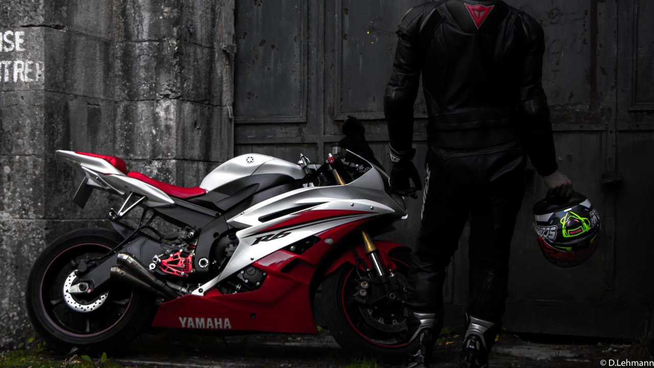 Man in Black Jacket and Black Pants Standing Beside Red and White Sports Bike. Wallpaper in 1280x720 Resolution