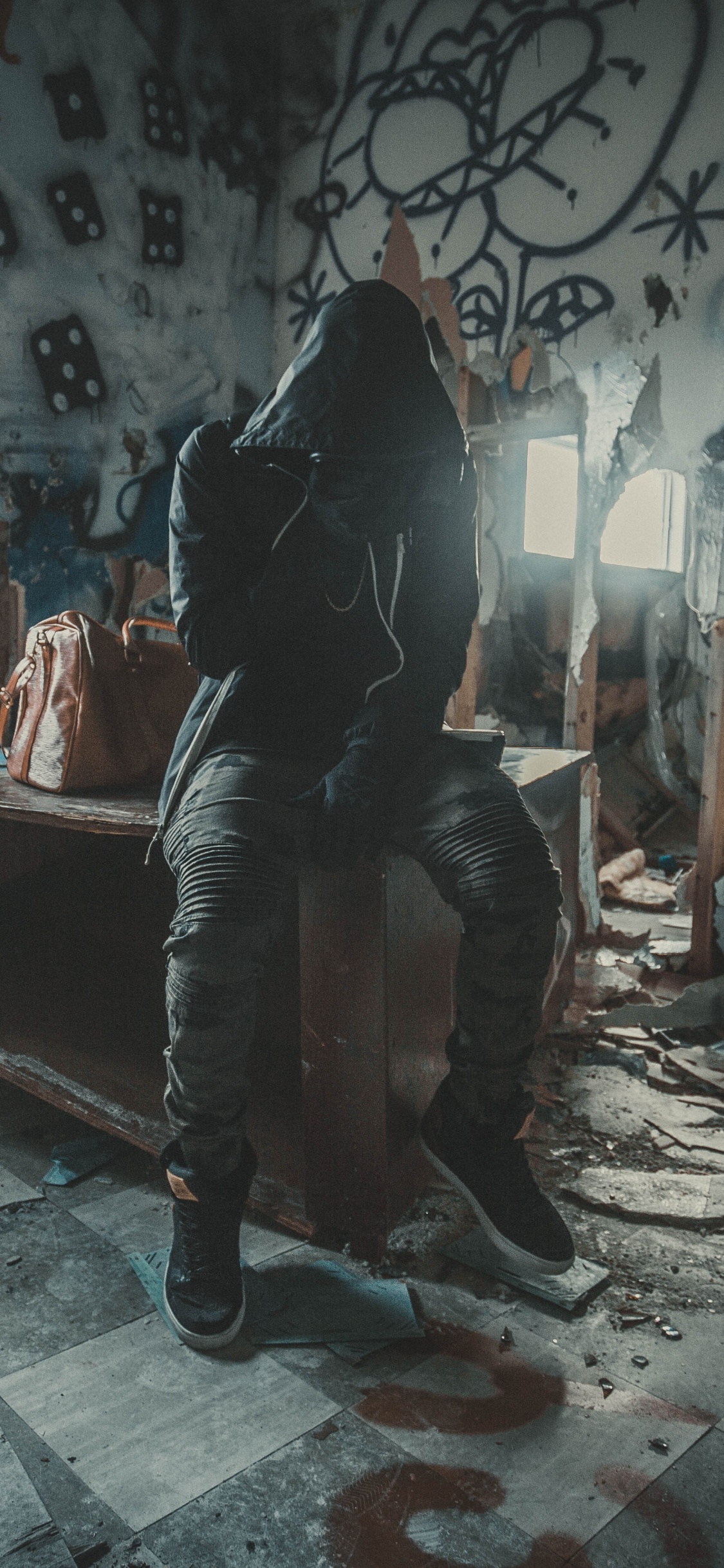 Mann in Schwarzer Jacke Sitzt Auf Brauner Holzbank. Wallpaper in 1125x2436 Resolution