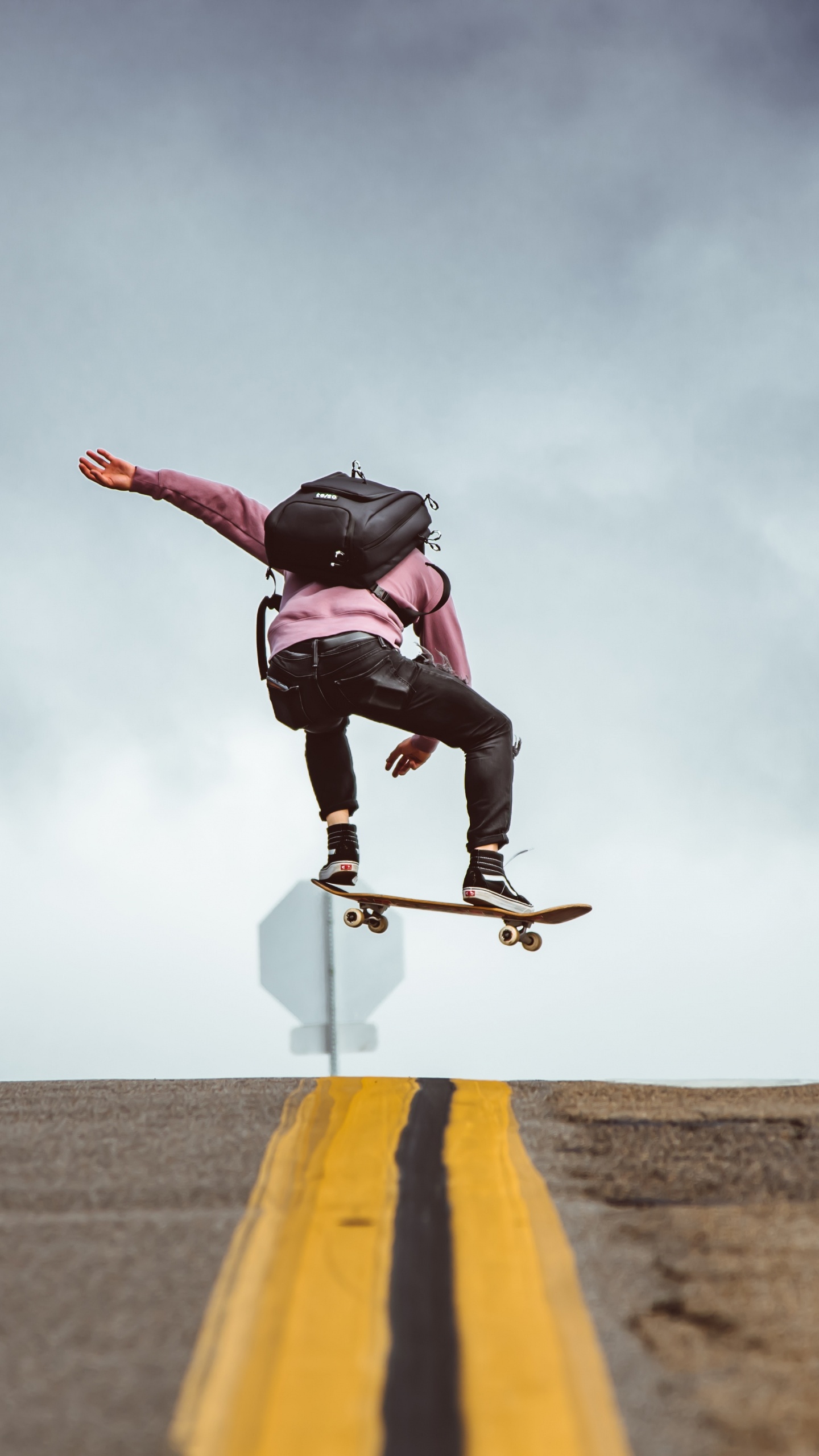 Man in Black Jacket and Black Pants Doing Stunts on Gray Asphalt Road Under Blue And. Wallpaper in 1440x2560 Resolution