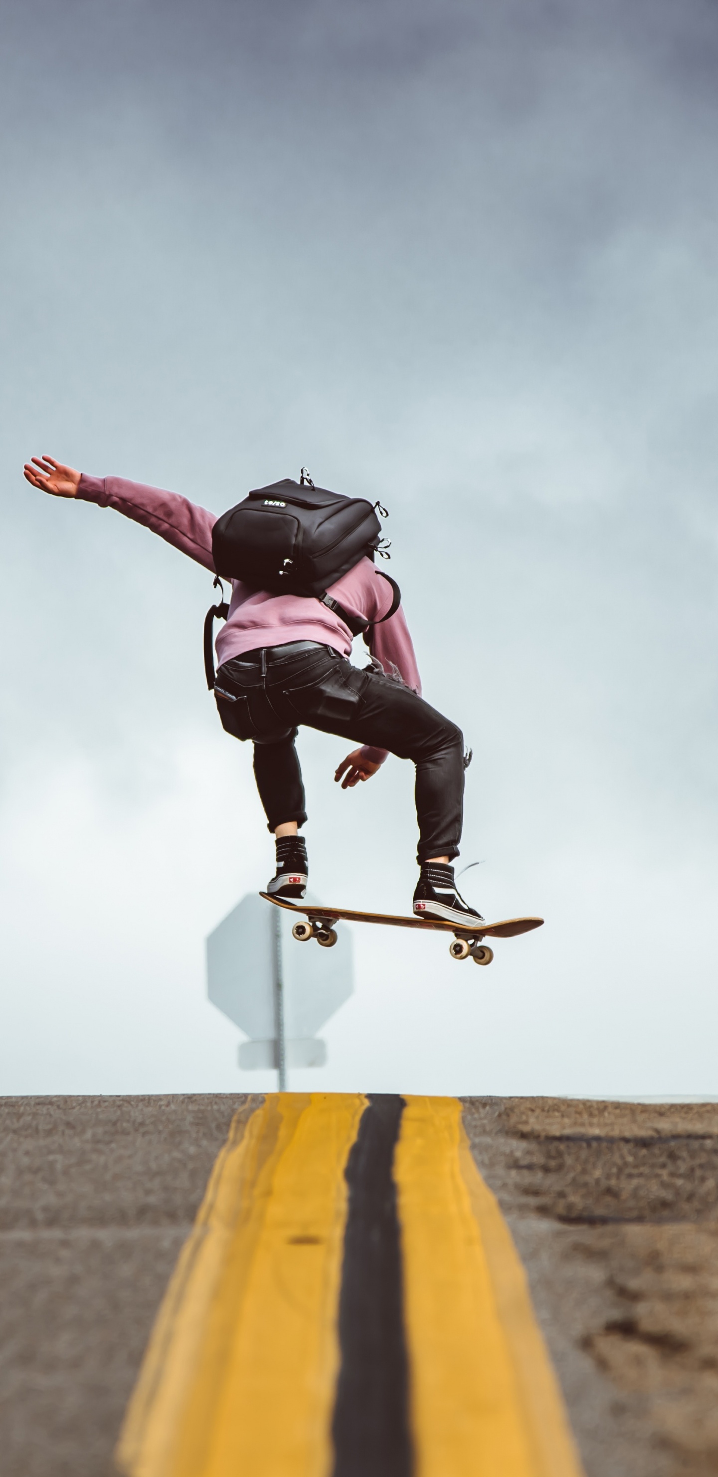 Man in Black Jacket and Black Pants Doing Stunts on Gray Asphalt Road Under Blue And. Wallpaper in 1440x2960 Resolution