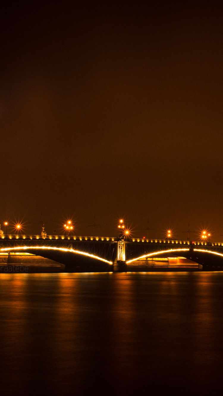 Beleuchtete Brücke Über Gewässer Während Der Nacht. Wallpaper in 750x1334 Resolution