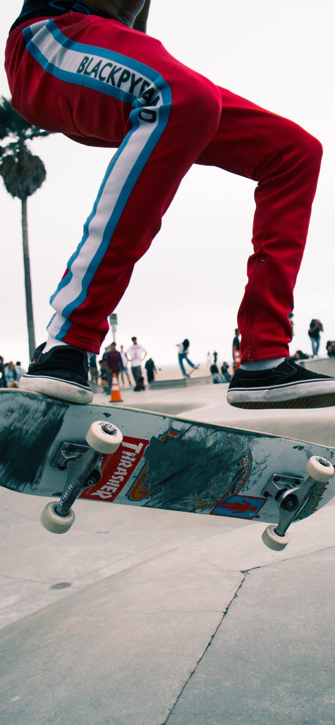 Man in Red Pants and Black and White Sneakers Riding Skateboard. Wallpaper in 1125x2436 Resolution