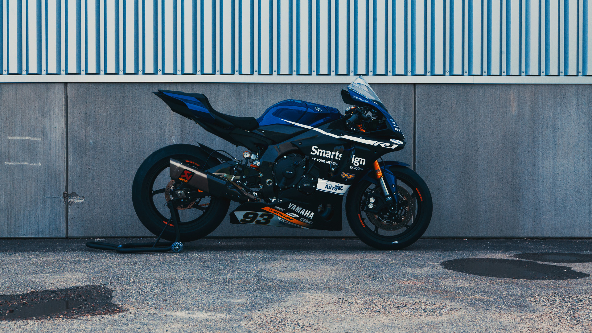 Black and Red Sports Bike Parked Beside Gray Roll up Door. Wallpaper in 1920x1080 Resolution