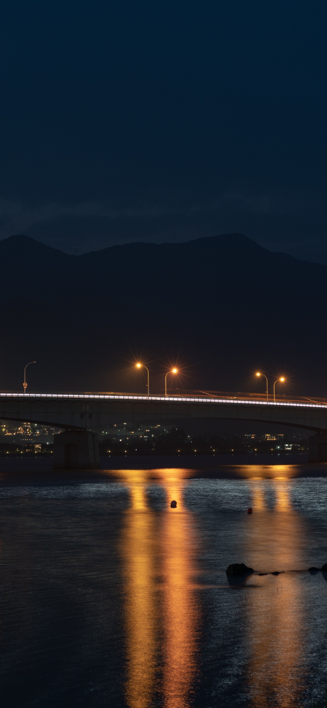 Beleuchtete Brücke Über Wasser Während Der Nacht Night. Wallpaper in 1125x2436 Resolution