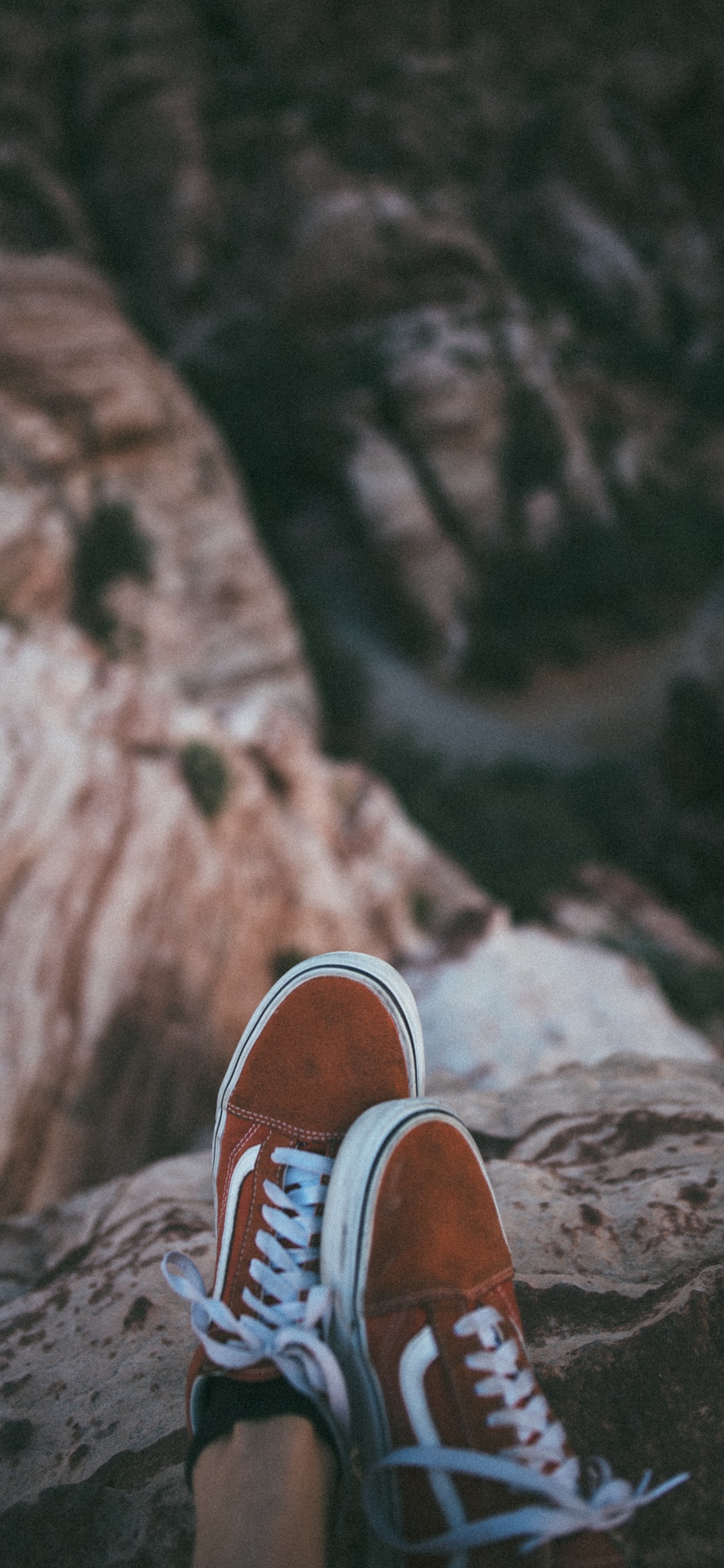 Persona en Zapatillas Marrones y Blancas Sentado Sobre la Formación Rocosa Durante el Día. Wallpaper in 1125x2436 Resolution