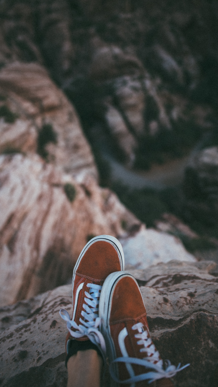 Person in Brown and White Sneakers Sitting on Rock Formation During Daytime. Wallpaper in 750x1334 Resolution