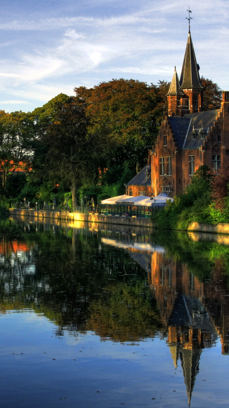 Brown Concrete Building Near Green Trees and Body of Water During Daytime. Wallpaper in 750x1334 Resolution