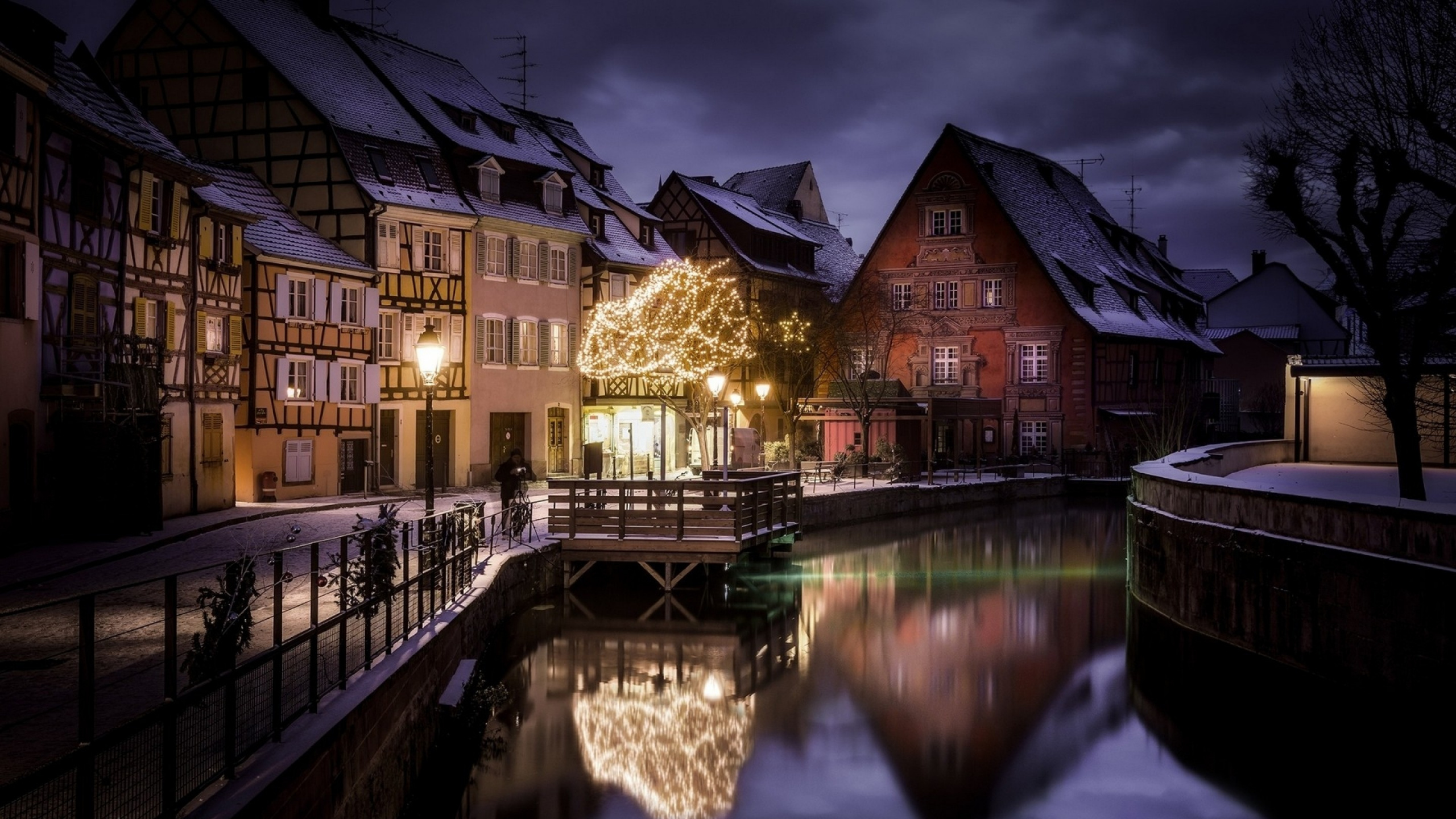 Braunes Und Schwarzes Betongebäude Neben Dem Fluss Während Der Nacht. Wallpaper in 2560x1440 Resolution