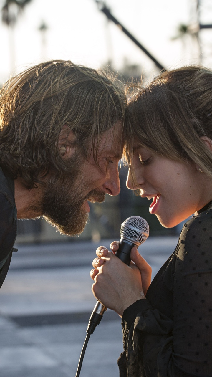 Man in Black Crew Neck T-shirt Holding Microphone Beside Woman in Black and White Polka. Wallpaper in 720x1280 Resolution