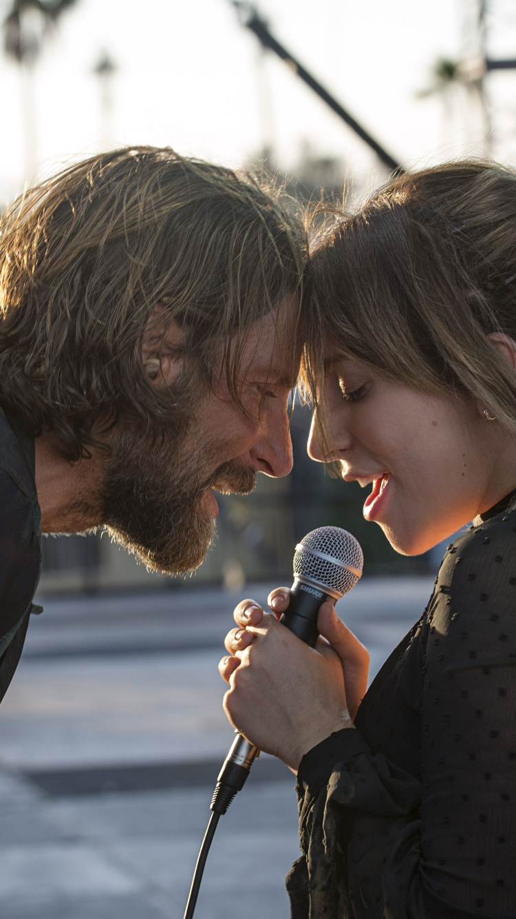 Hombre en Camiseta Negra Con Cuello Redondo Sosteniendo Micrófono Junto a Una Mujer en Polka Blanco y Negro. Wallpaper in 750x1334 Resolution