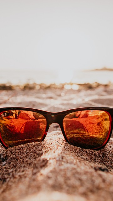 Image black framed sunglasses on beach during sunset