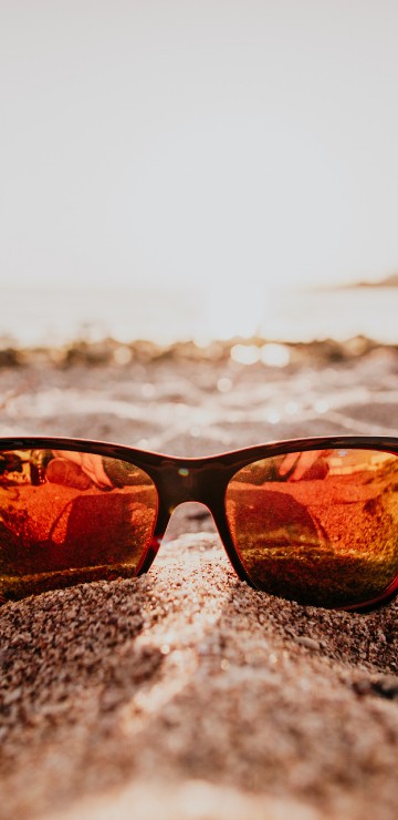Image black framed sunglasses on beach during sunset