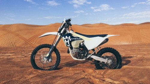 Image white and black motocross dirt bike on brown sand under blue sky during daytime