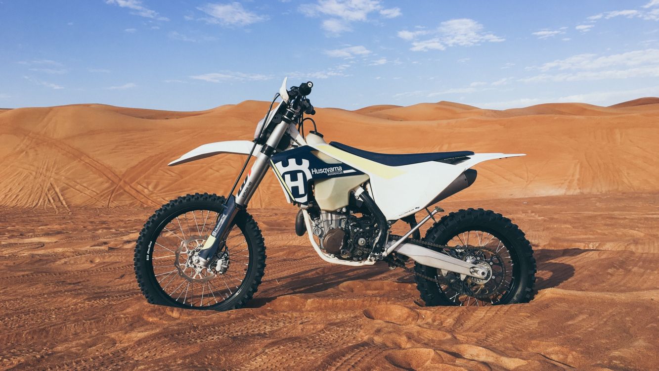 white and black motocross dirt bike on brown sand under blue sky during daytime