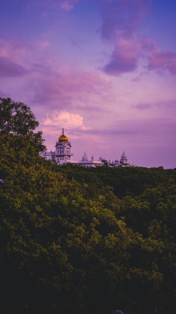 Image white and brown concrete building surrounded by green trees under cloudy sky during daytime