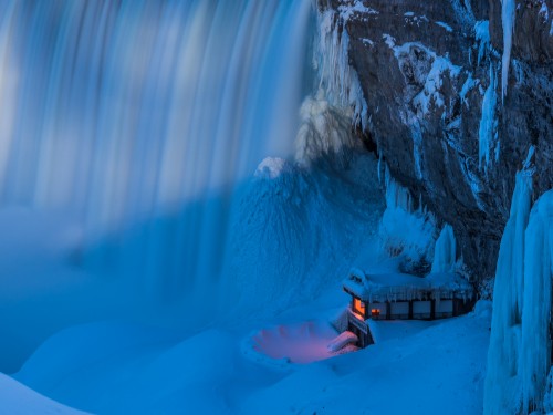 Image person in orange jacket sitting on brown wooden dock near white snow covered mountain during daytime