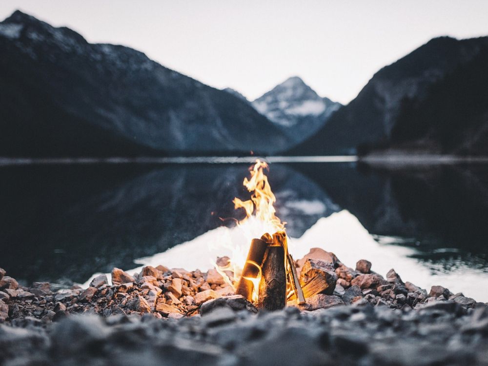 bonfire on rocky shore near lake during daytime