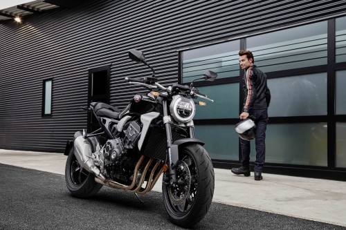 Image man in black jacket standing beside black and silver cruiser motorcycle