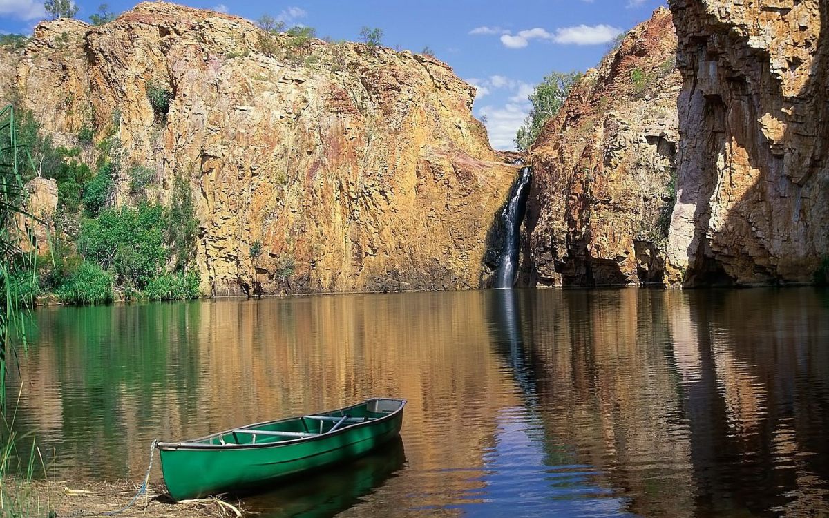 green boat on lake near brown rocky mountain during daytime