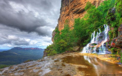 Image water falls between brown rocky mountain under gray cloudy sky during daytime