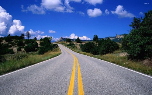 Image gray concrete road between green grass field under blue sky and white clouds during daytime