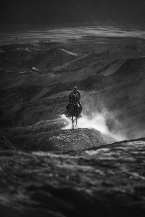 Image grayscale photo of man in black jacket and pants standing on rock formation