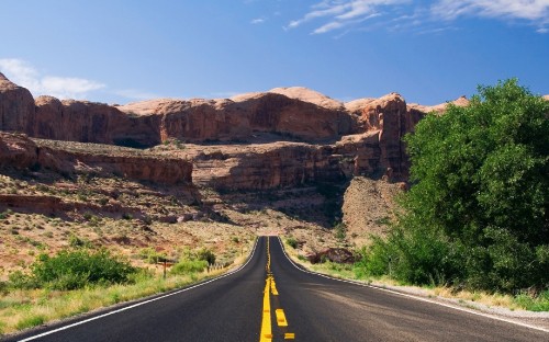 Image gray asphalt road between brown rock formation under blue sky during daytime