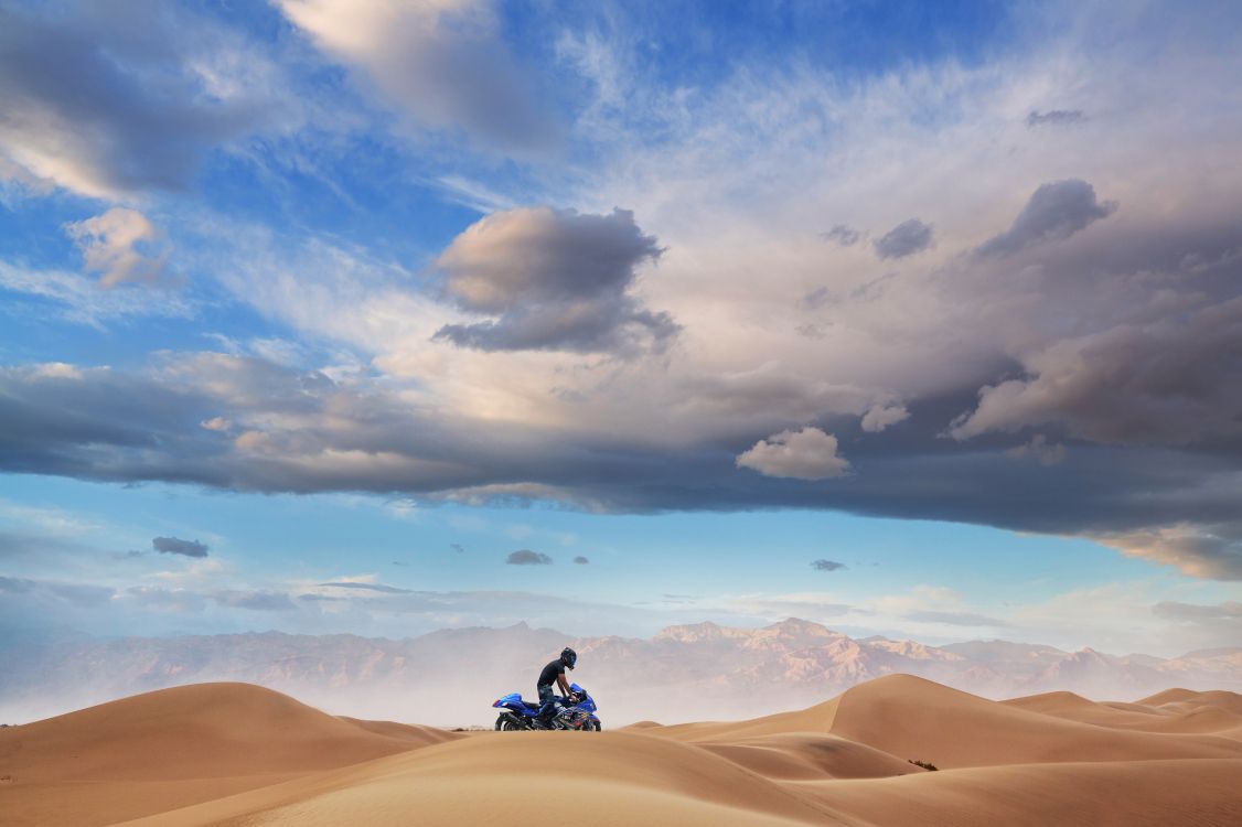 Man in Black Jacket and Black Pants Sitting on Brown Sand Under Blue Sky During Daytime. Wallpaper in 5600x3728 Resolution