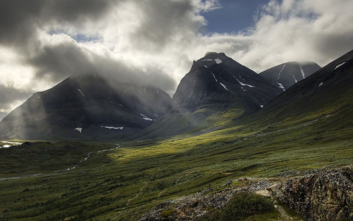 green grass field near mountain under cloudy sky during daytime