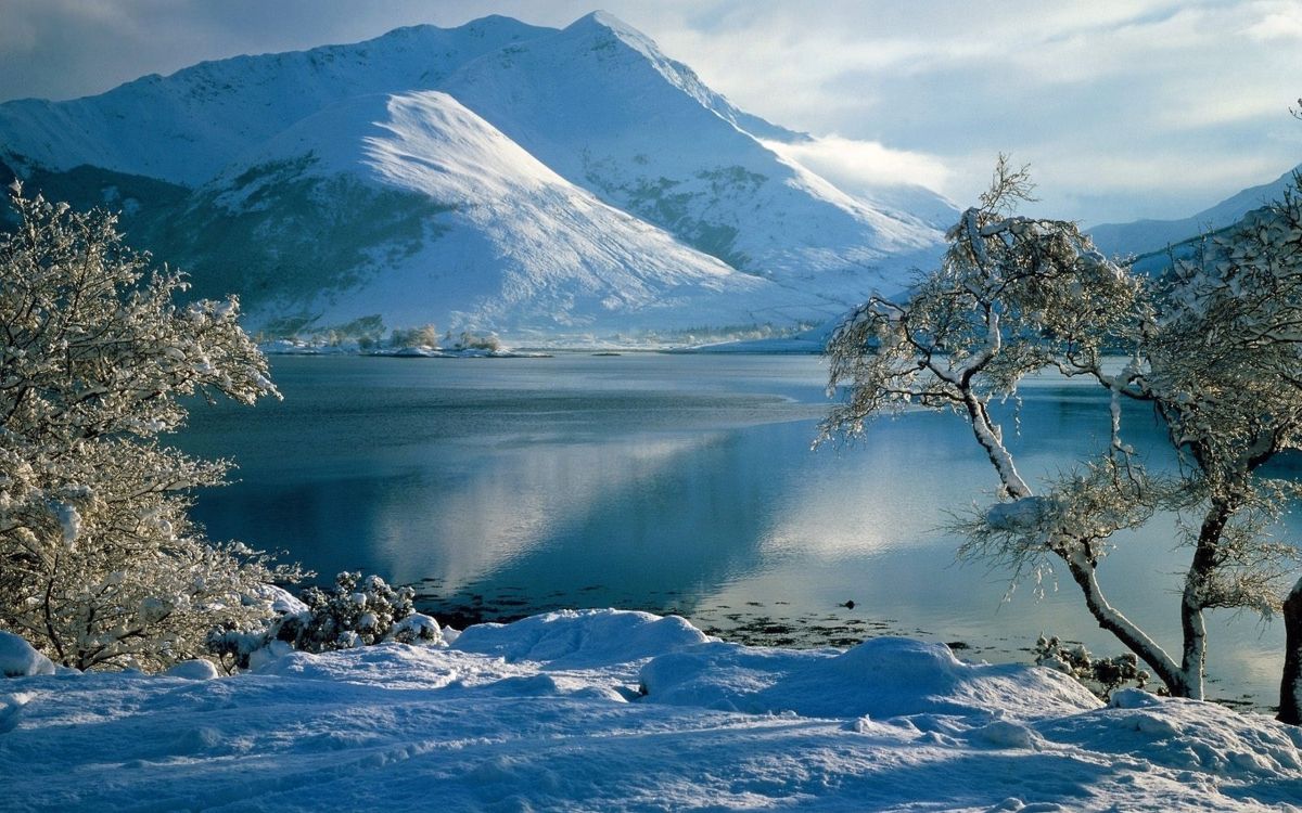 snow covered mountain near body of water during daytime