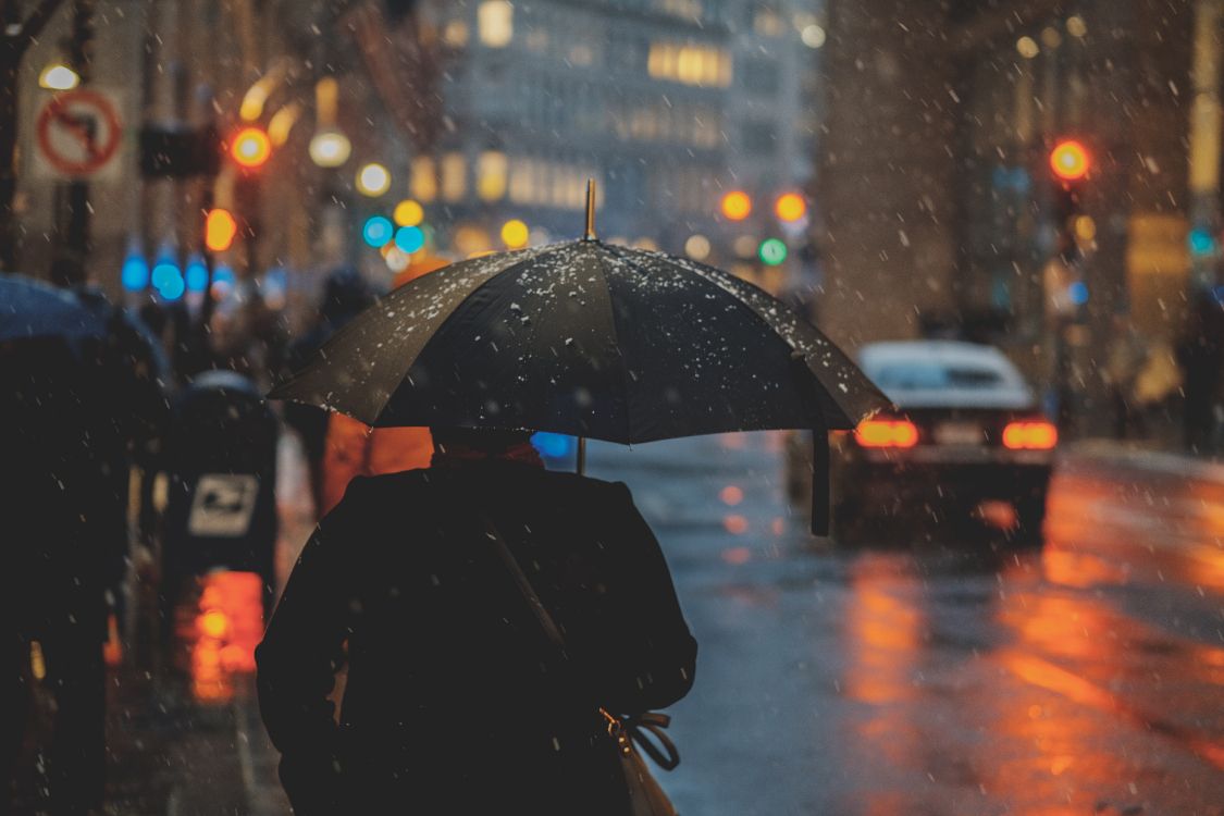 person in black coat holding umbrella during rain