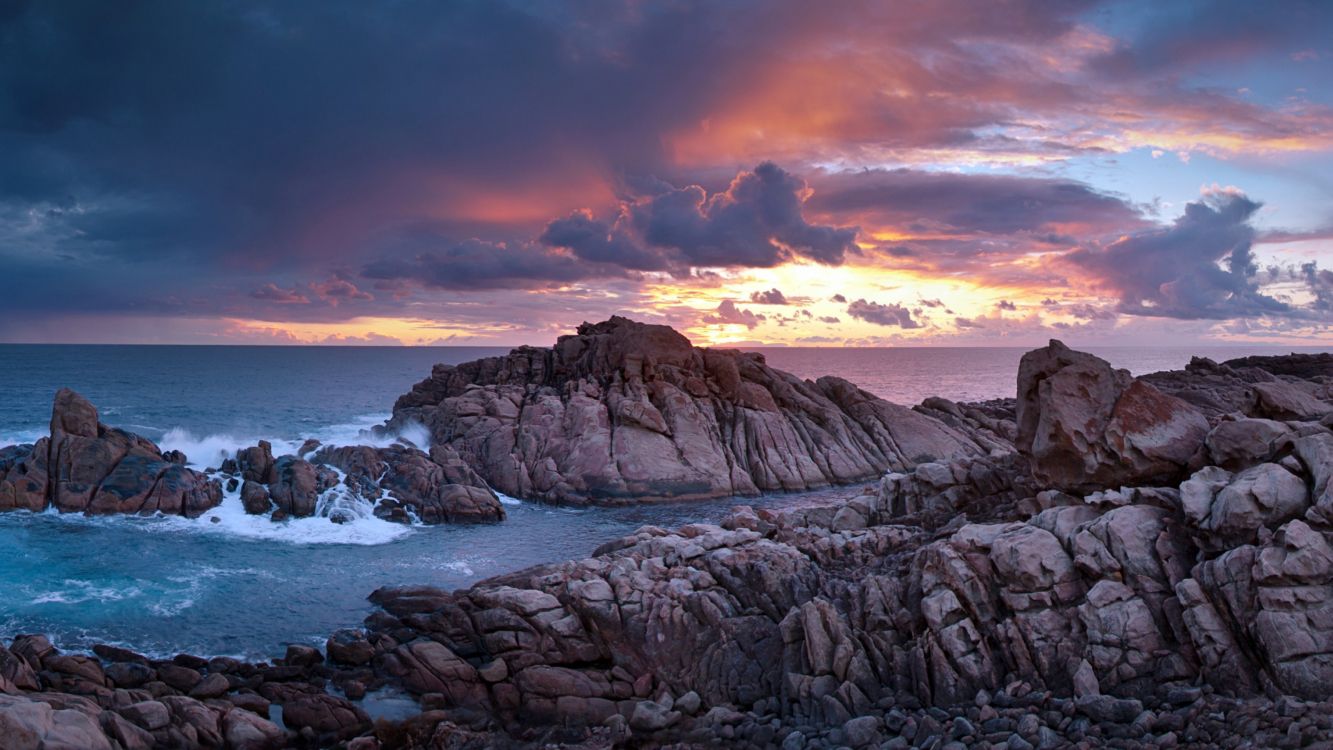 brown rock formation near body of water during sunset