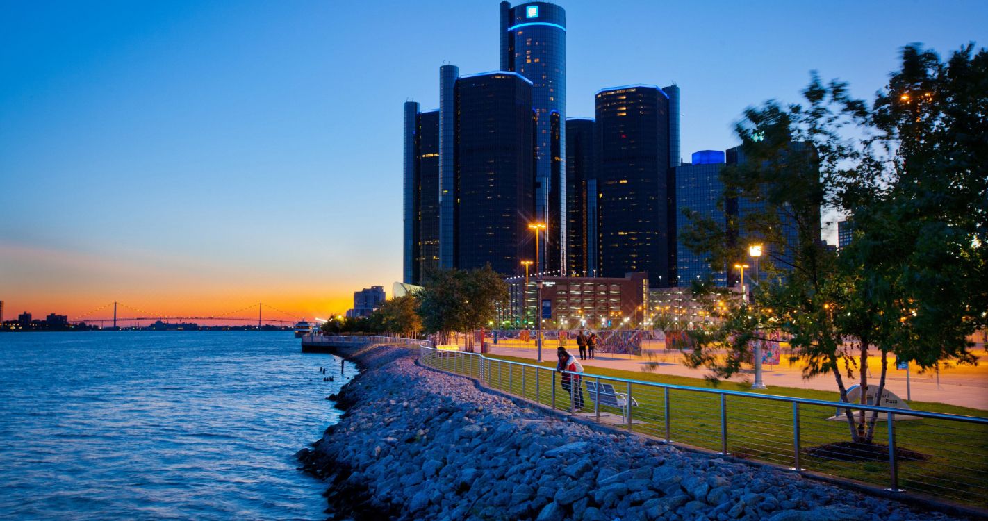 people walking on sidewalk near body of water during sunset