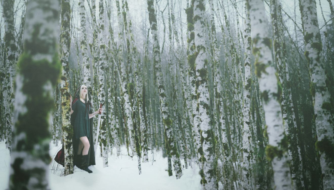 woman in black dress standing on snow covered ground near green trees during daytime