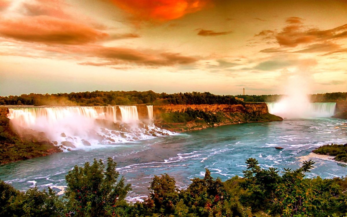 waterfalls near green trees under cloudy sky during daytime