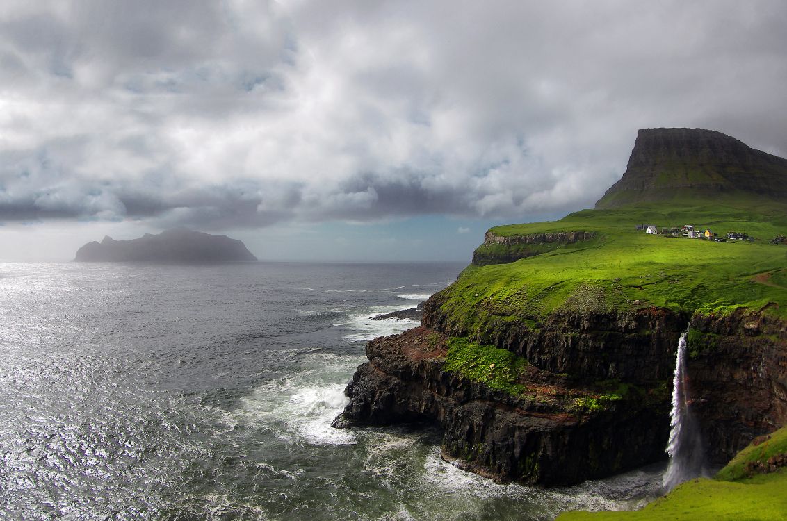 green and brown mountain beside sea under cloudy sky during daytime