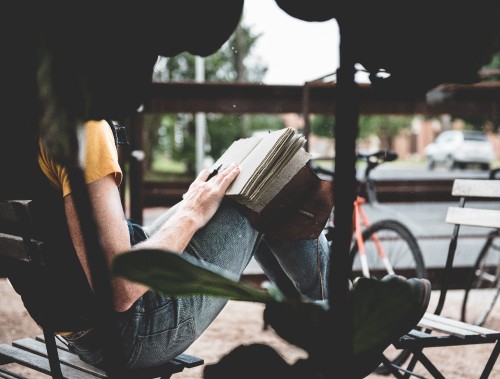 Image man in black t-shirt and blue denim jeans sitting on chair reading book