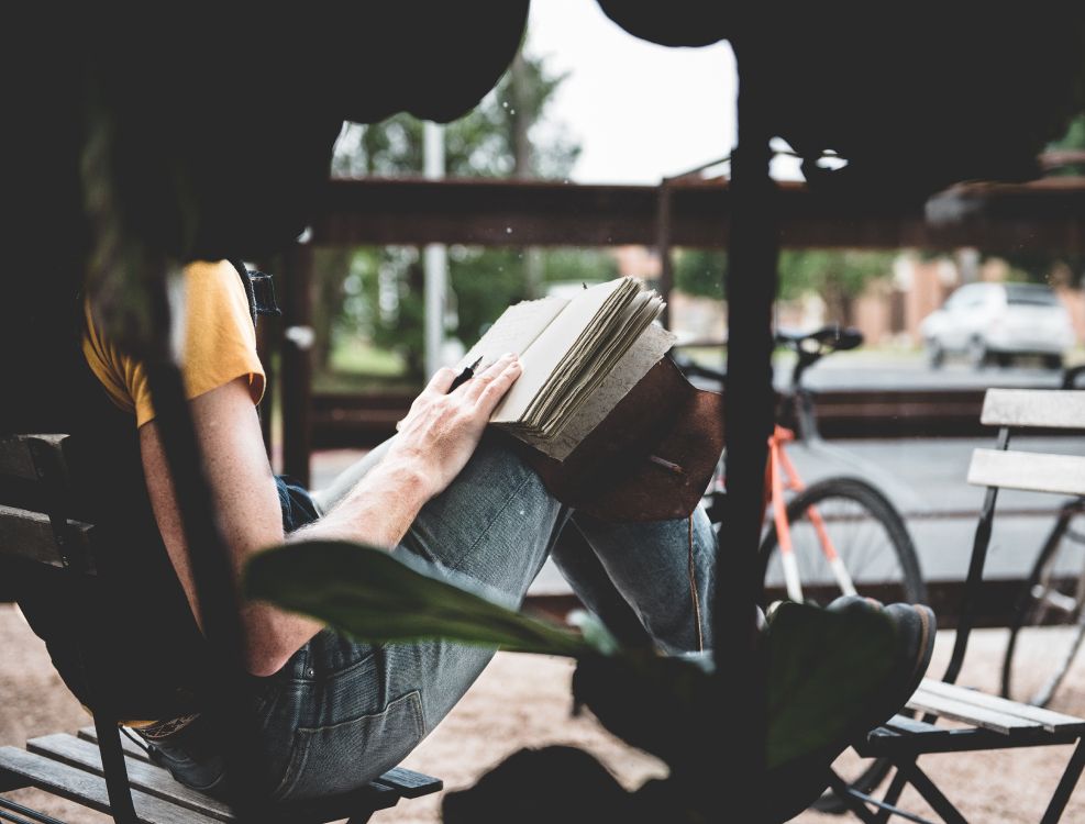 man in black t-shirt and blue denim jeans sitting on chair reading book