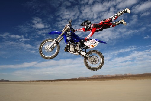 Image man riding motocross dirt bike on brown sand under blue sky during daytime