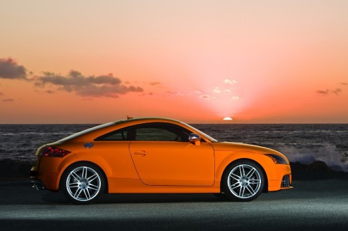 Image yellow porsche 911 on gray concrete pavement near body of water during sunset