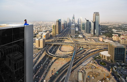 Image man in blue jacket sitting on top of building looking at city buildings during daytime