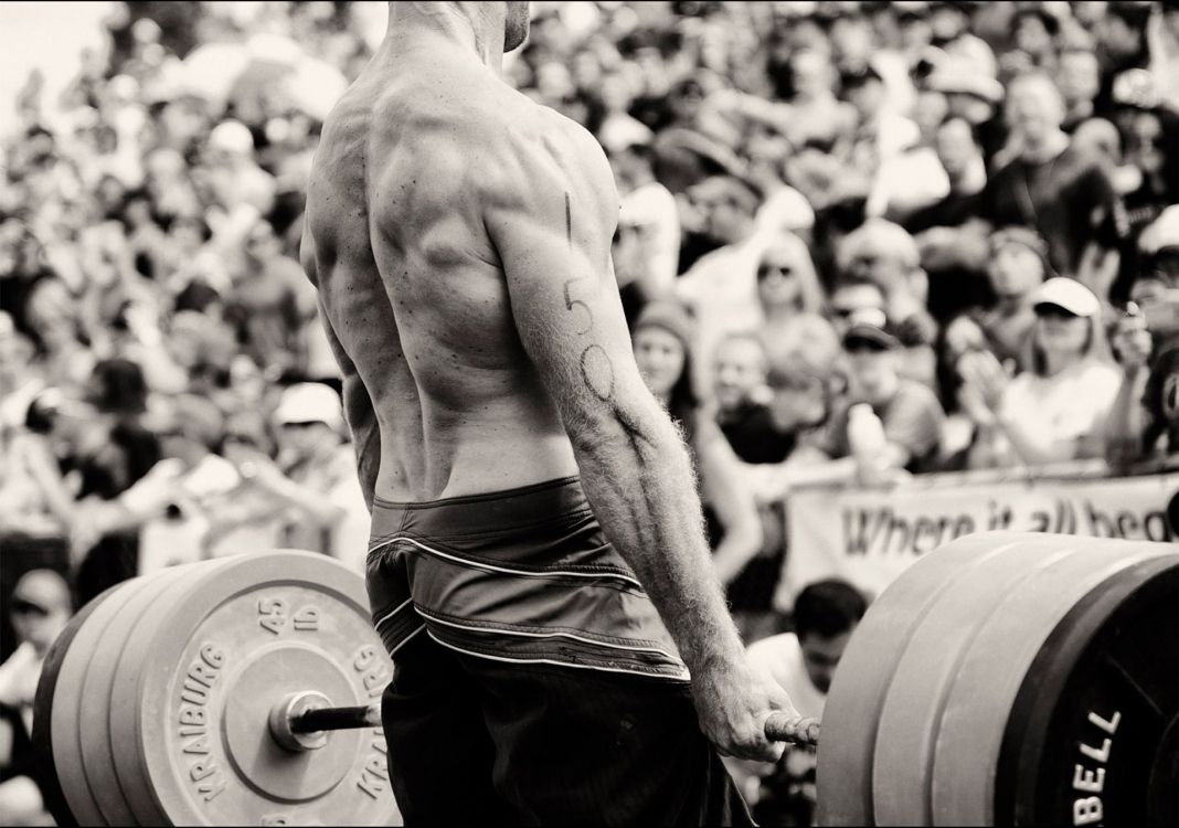 topless man in black shorts carrying barbell