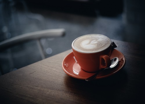 Image red ceramic mug with coffee on orange saucer