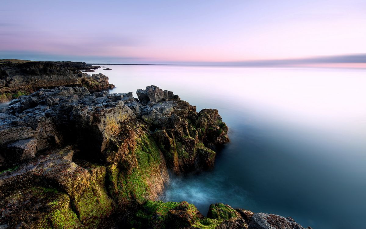 brown and green rock formation beside body of water