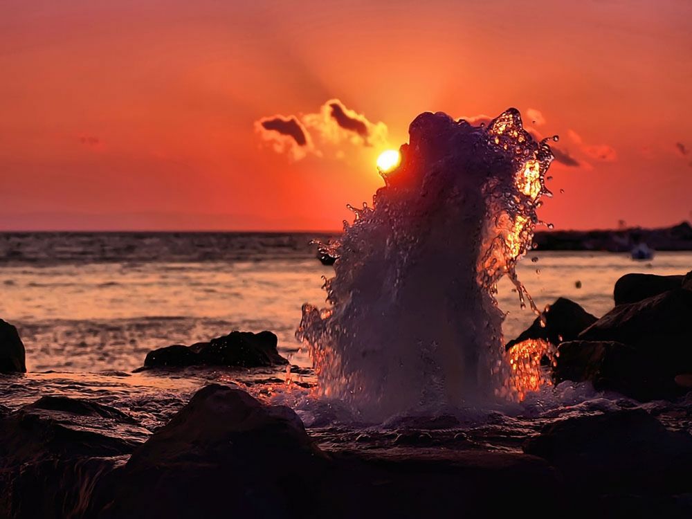 silhouette of person standing on rock near body of water during sunset