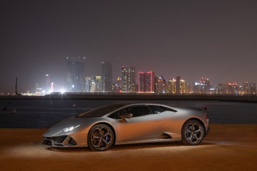 Image white coupe parked on brown field near city buildings during night time