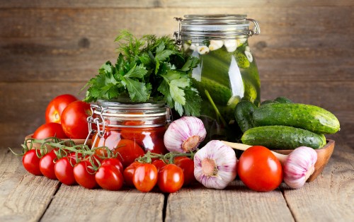 Image red tomatoes and green leaves in clear glass jar